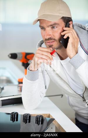 uomo in piedi in cucina che parla sul telefono cellulare Foto Stock