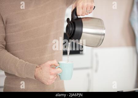 la persona versa l'acqua dal bollitore in cucina Foto Stock