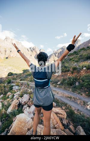 Vista posteriore della giovane donna in piedi in valle con braccia sollevate. Giovane donna che ama fare un'escursione. Foto Stock
