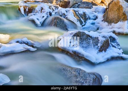 Particolare di acqua che versa attraverso rocce ricoperte di gelo dalla primavera precoce Foto Stock