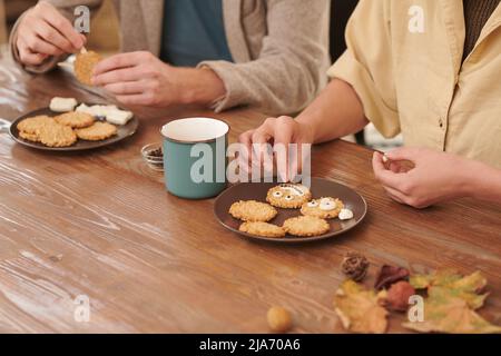 Primo piano di coppia irriconoscibile seduta a tavola con foglie d'autunno e decorazione biscotti di zucchero per Halloween Foto Stock