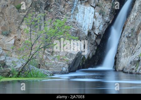 Cascata di montagna nella Sierra de Madrid che scorre tra le scogliere rocciose in una piscina limpida, catturata con una lunga esposizione in un tranquillo paesaggio naturale Foto Stock