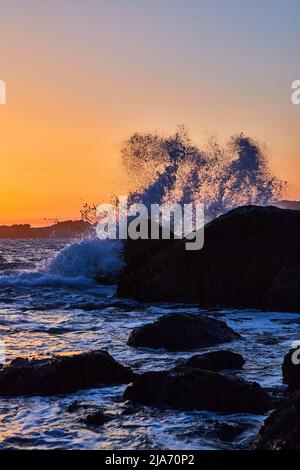 Ora d'oro sull'oceano con grande onda che si schiantano sulle rocce Foto Stock