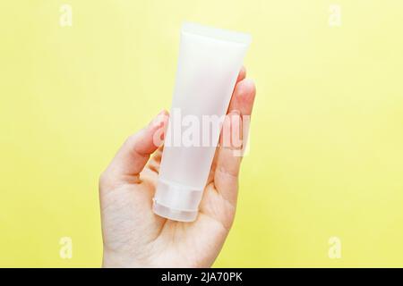 Donna mano che tiene crema tubo prodotti cosmetici su uno sfondo giallo. Foto Stock