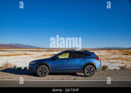 Blue Subaru Crosstrek parcheggiato su strada con deserto di sabbia bianca sullo sfondo fuori Death Valley Foto Stock