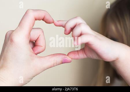Forma del cuore creata dalle mani della bambina e dalle mani della madre sullo sfondo beige. Concetto di amore, felicità e sicurezza. Foto Stock