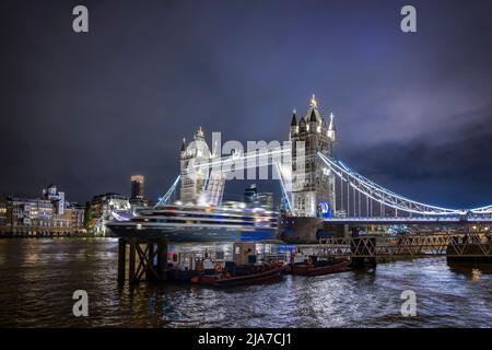 Vista notturna dello skyline di Londra con una nave da crociera che passa sotto il Ponte della Torre sollevato Foto Stock