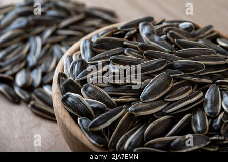 Semi di girasole neri in una ciotola su sfondo di legno Foto Stock