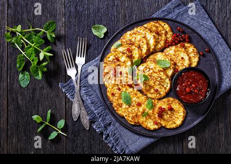 pancake di farina di farro dolce con salsa di bacca, mirtillo di montagna, cowberry su piatto nero su tavola di legno scuro, vista orizzontale dall'alto, piatto, Foto Stock