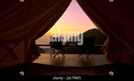 Tenda turistica in campo tra con vista sulle montagne all'alba. Vista dal campeggio tenda su incredibile alba con montagne e due sedie da campeggio pieghevoli Foto Stock