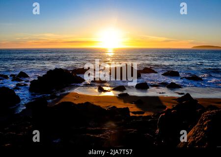 Ombre scure che scondano sulle rocce disperse dell'Oceano mentre il sole tramonta sotto l'orizzonte. Preso a Bodega Bay, California. Foto Stock