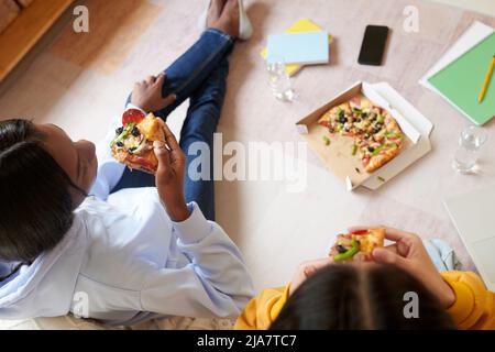 Ragazze adolescenti che mangiano la pizza dopo aver finito con i compiti, vista dall'alto Foto Stock