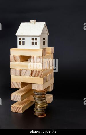 Casa modello in cima ad una torre di blocchi di legno, sostenuta da un'alta pila di monete Foto Stock