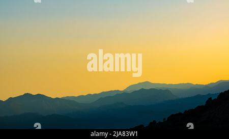 Splendida vista sulle colline o sulle montagne al tramonto. Colline coperte di foresta stratificata. Sfondo banner. Foto Stock