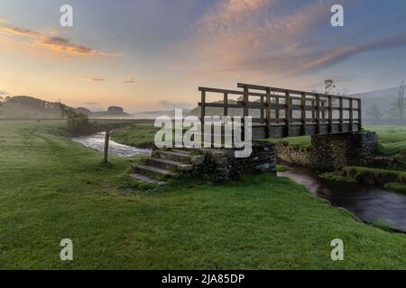 Alba sul ponte pedonale sopra Gayle Beck vicino alla pittoresca cittadina di Hawes, nel Parco Nazionale Yorkshire Dales, North Yorkshire, Inghilterra. Foto Stock