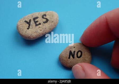 La mano sceglie una pietra con il testo No. Pietra con la parola Sì su una tavola blu. Concetto di scelta Foto Stock