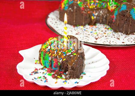 Candela di compleanno in una fetta di torta al cioccolato arcobaleno Foto Stock