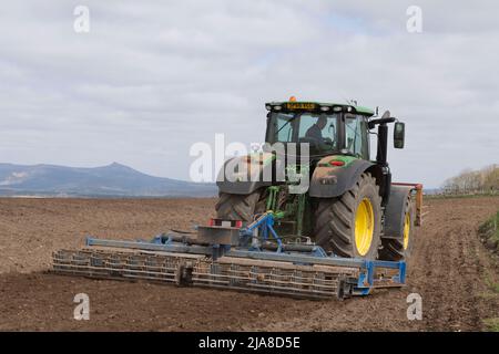 Un contadino nell'Aberdeenshire che coltiva un campo arato in primavera con Bennachie visibile in lontananza Foto Stock