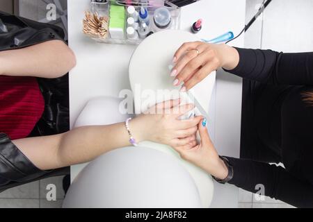 Closeup colpo di una donna in una manicure ricevendo una manicure da un estetista con lima per unghie. Donna ottenere unghie manicure. Estetista file chiodi ad un c Foto Stock