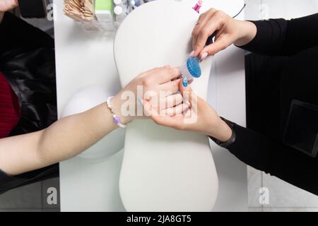 Il primo piano delle mani del manicurista sta rimuovendo la polvere dalle unghie con un pennello per pulire le unghie nel salone del manicure. Il manicurista rimuove la polvere acrilica dalla Th Foto Stock