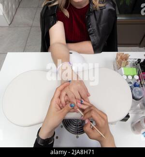 Primo piano di mani esteticiste pulizia unghie con attrezzatura. Mani di donna che ricevono trattamento manicure. Primo piano del manicurista che spinge le cuticole sul chiodo Foto Stock