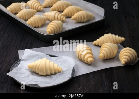 Crudo croissant non cotto su carta da forno in rustico PlateOver Nero tavolo di legno sfondo Foto Stock