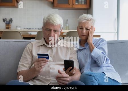 Scioccato coppia anziano overspending soldi in linea usando il telefono della carta di credito Foto Stock