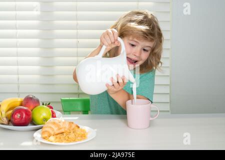 Il ragazzo piccolo di Fuuny versa il latte intero delle mucche per colazione. Bambino ragazzo che mangia cibo sano biologico. Verdure sane con vitamine. Nutrizione adeguata dei capretti Foto Stock