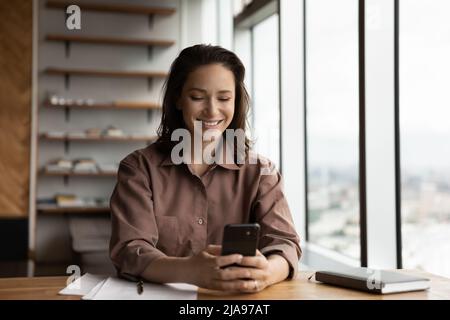 Dipendente felice femmina che legge il messaggio di testo sullo schermo della cella Foto Stock