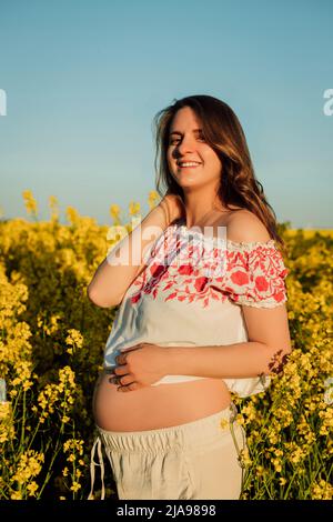 Una donna incinta in una camicia ricamata Ucraina si trova in un campo di colza Foto Stock