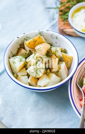 Insalata di patate con aneto e olive in una ciotola su sfondo blu. Cibo sano, vegano e ricette magre. Foto Stock