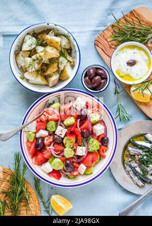 Scena da tavola greca, vista dall'alto . Varietà di piatti tra cui insalata greca, cetriolo tuffo Tzatziki, filetti di anchovy, patate al limone. Foto Stock