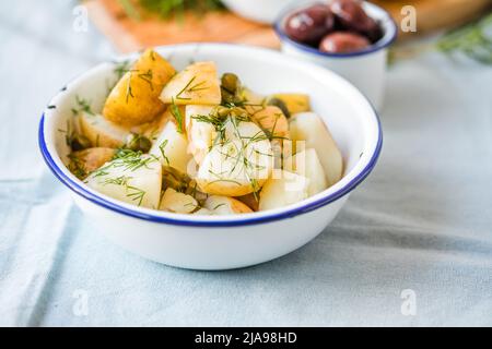 Insalata di patate con aneto e olive in una ciotola su sfondo blu. Cibo sano, vegano e ricette magre. Foto Stock