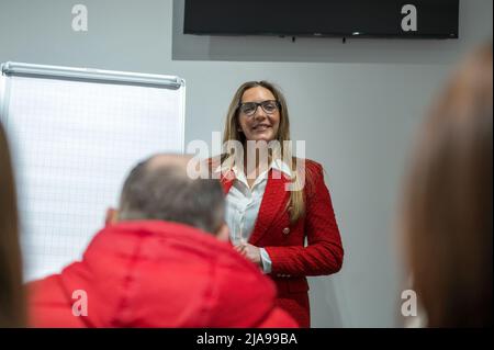 RIVNE, UCRAINA - 22 FEBBRAIO 2022. Donna in giacca rossa con una presentazione aziendale. Donna d'affari attraente in giacca rossa in piedi vicino a flipch Foto Stock