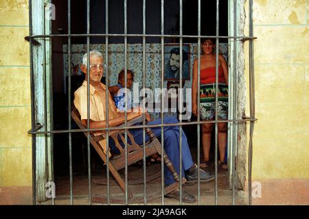 Vecchio uomo in una sedia a dondolo dietro una finestra barred, città vecchia di Trinidad, patrimonio mondiale dell'UNESCO, Cuba, Caraibi Foto Stock