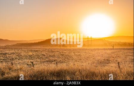 Le tonalità dorate si estendono in un paese bruciato dal sole, dove la luce finale della giornata bacia la terra, dipingendo il cielo con sfumature di arancione e giallo Foto Stock