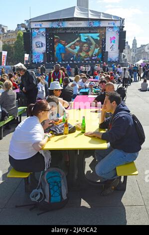 Primo piano di persone ai tavoli da picnic dipinti a Trafalgar Square di fronte al grande schermo TV durante i giochi olimpici e paraolimpici di Londra 2012 Inghilterra Regno Unito Foto Stock