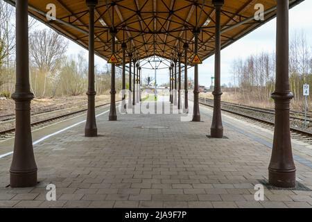 Piattaforma coperta con colonne d'epoca, ponteggi in metallo e tetto in legno tra le rotaie della stazione di Schonberg, Mecklenburg, Germania Foto Stock