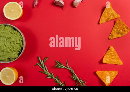 Composizione di guacamole con gli ingredienti per la sua creazione e il nachos per il suo consumo su sfondo rosso. Foto Stock