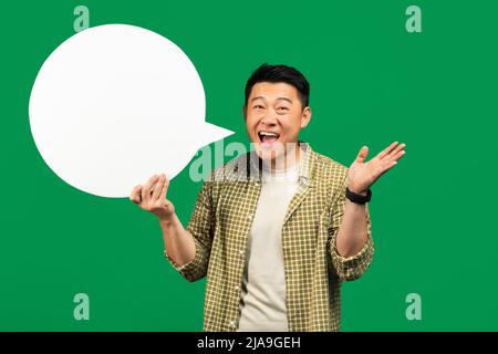 Notizie, dialogo, concetto di annuncio. Felice asiatico uomo maturo tenendo vuoto bolla discorso su sfondo verde, mockup Foto Stock