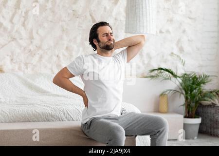 Uomo infelice che soffre di mal di schiena a casa in camera da letto Foto Stock