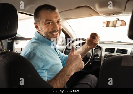 Uomo felice seduto in auto mostrando le chiavi gesturando pollici in su Foto Stock