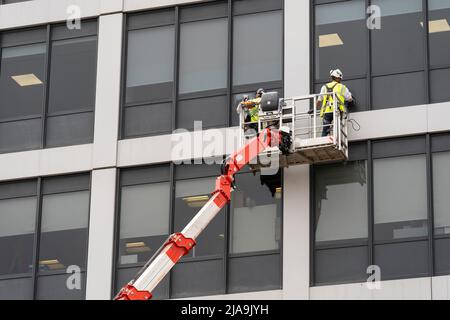 Uomini che lavorano in una piattaforma di lavoro mobile sopraelevata (MEWP) che indossano PPE personali e finestre di pulizia su un ufficio a più piani a Basingstoke. Inghilterra Foto Stock