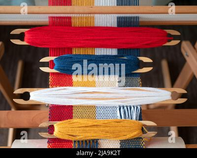 Quattro navette con filo di diversi colori sul telaio. Navette di tessitura con fili blu, bianco, rosso e giallo sul progetto di tessitura Foto Stock