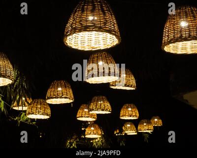 Molte lampade con paralumi in vimini illuminano il vicolo di bambù scuro nel parco. Foto Stock