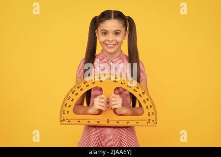 felice bambino tenere la scuola matematico strumento righello protactor su sfondo giallo, la scuola Foto Stock