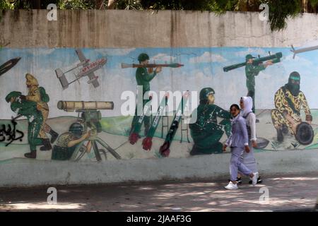 Khan Younis, Gaza. 29th maggio 2022. I palestinesi camminano davanti a un murale raffigurante combattenti che sparano razzi nella città di Khan Younis nella striscia meridionale di Gaza domenica 29 maggio 2022. Gerusalemme si sta preparando a una controversa "marcia di bandiera” da parte degli israeliani che ha scatenato l'allarme di una nuova escalation da parte delle fazioni palestinesi. Foto di Ismael Mohamad/UPI Credit: UPI/Alamy Live News Foto Stock