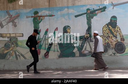 Khan Younis, Gaza. 29th maggio 2022. I palestinesi camminano davanti a un murale raffigurante combattenti che sparano razzi nella città di Khan Younis nella striscia meridionale di Gaza domenica 29 maggio 2022. Gerusalemme si sta preparando a una controversa "marcia di bandiera” da parte degli israeliani che ha scatenato l'allarme di una nuova escalation da parte delle fazioni palestinesi. Foto di Ismael Mohamad/UPI Credit: UPI/Alamy Live News Foto Stock