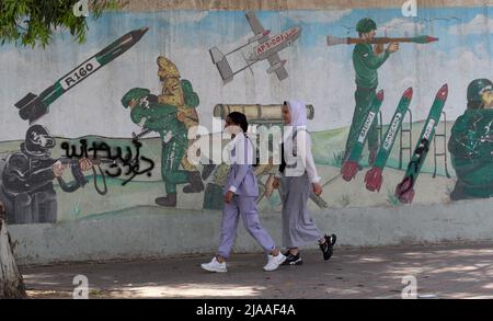 Khan Younis, Gaza. 29th maggio 2022. I palestinesi camminano davanti a un murale raffigurante combattenti che sparano razzi nella città di Khan Younis nella striscia meridionale di Gaza domenica 29 maggio 2022. Gerusalemme si sta preparando a una controversa "marcia di bandiera” da parte degli israeliani che ha scatenato l'allarme di una nuova escalation da parte delle fazioni palestinesi. Foto di Ismael Mohamad/UPI Credit: UPI/Alamy Live News Foto Stock