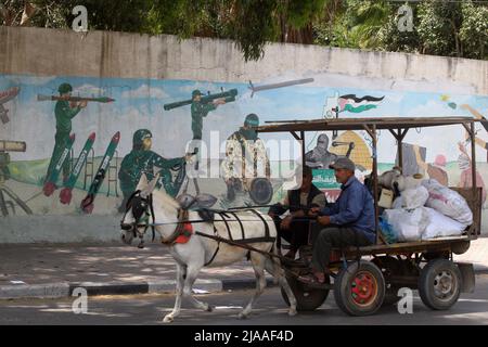 Khan Younis, Gaza. 29th maggio 2022. I palestinesi camminano davanti a un murale raffigurante combattenti che sparano razzi nella città di Khan Younis nella striscia meridionale di Gaza domenica 29 maggio 2022. Gerusalemme si sta preparando a una controversa "marcia di bandiera” da parte degli israeliani che ha scatenato l'allarme di una nuova escalation da parte delle fazioni palestinesi. Foto di Ismael Mohamad/UPI Credit: UPI/Alamy Live News Foto Stock